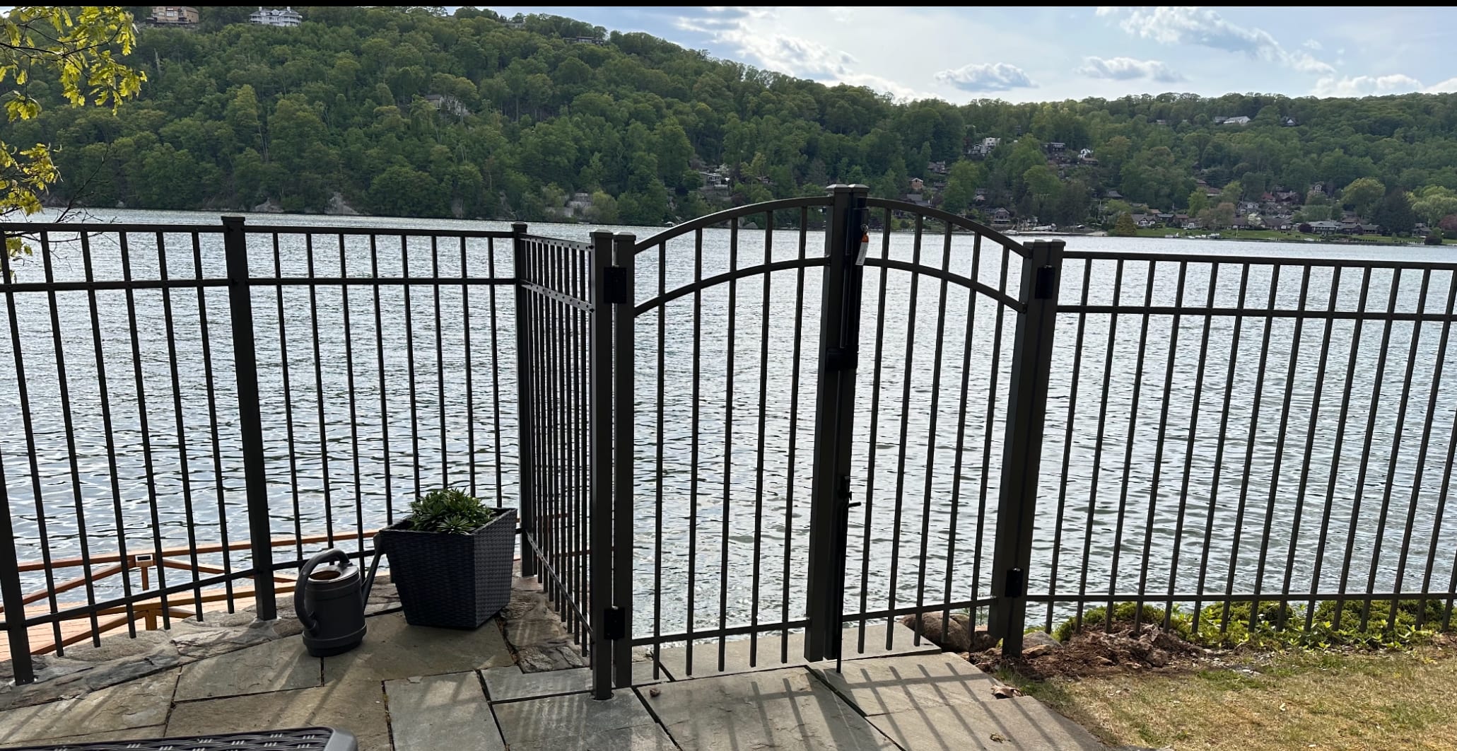 Bronze aluminum fence with an arched-top gate on a stone patio overlooking a lake and wooded hillside