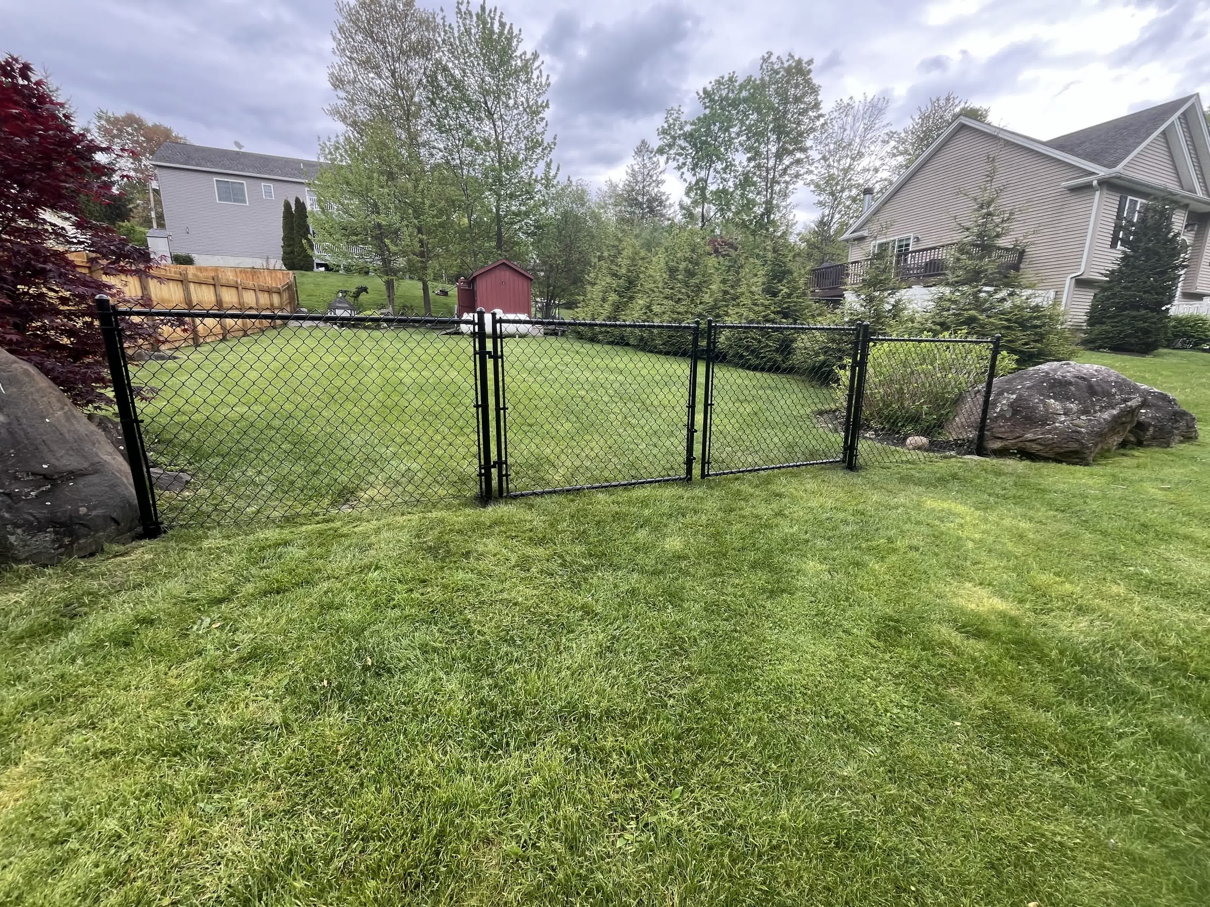 Black chain-link fence with a swing gate enclosing a level backyard between two houses
