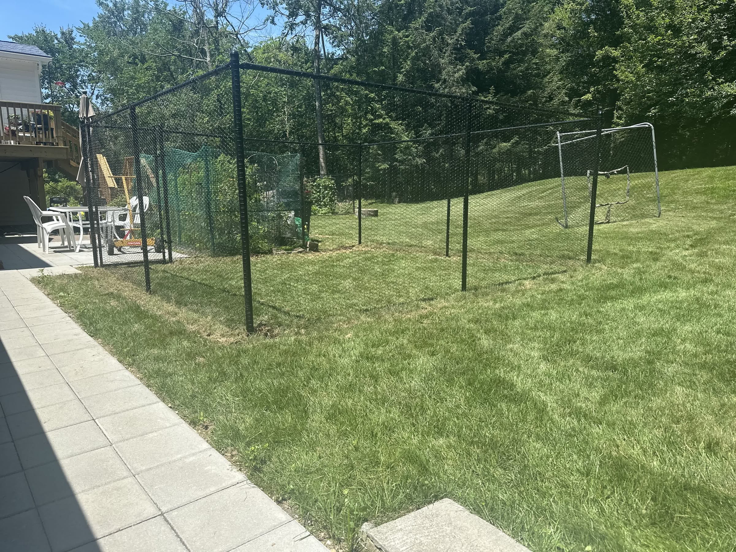 Tall black chain-link enclosure surrounding a backyard garden area next to a paver walkway