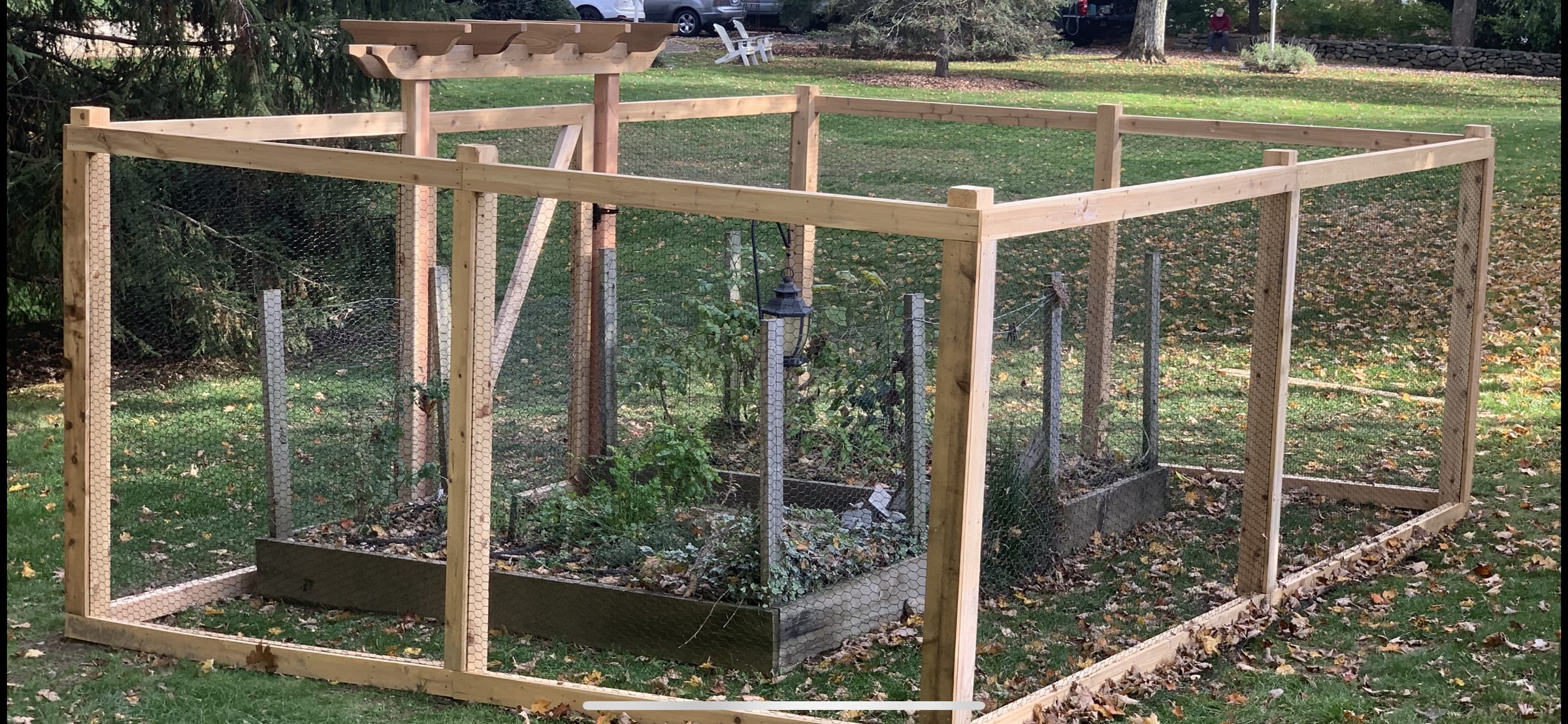 Cedar-framed garden fence with chicken wire and a pergola arbor over the gate, on an autumn lawn.