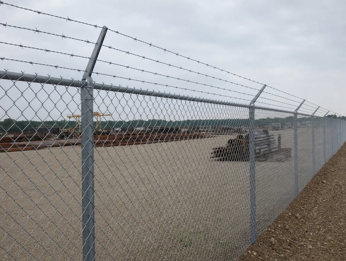 A six foot chain link fence topped with barbed wire around an industrial yard